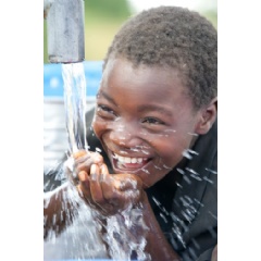 While drinking water from a hand pump, a child smiles, in Mzuzu, the capital of Northern Region and the third largest city, by population, in Malawi.